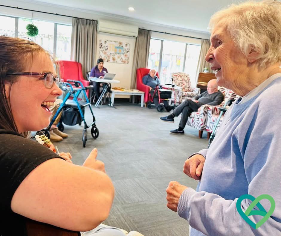 Joanna and a resident laughing together during a group music session in a rest home lounge